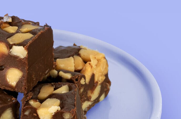 Three squares of nut filled chocolate fudge on a blue plate against a matching blue surface.