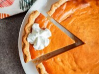 Una tarta de calabaza sobre un plato con una porción cortada con crema batida por encima.