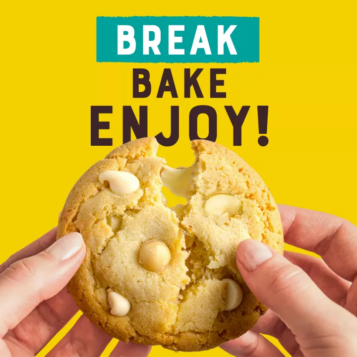 Vista del ángulo izquierdo de un paquete amarillo y blanco que muestra el logotipo NESTLÉ® TOLL HOUSE® con una etiqueta verde azulada que dice "masa de galletas de nueces de macadamia con trocitos blancos" y 2 galletas de nueces de macadamia con trocitos blancos encima de una superficie blanca.