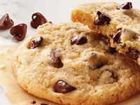 Pila de galletas de chispas de chocolate sobre una bolsa marrón, una galleta partida por la mitad con chispas derretidas.