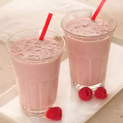 Photograph: two creamy raspberry milkshakes in tall glasses with red straws and raspberries.