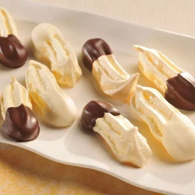 Photograph of meringue cookies dipped in dark chocolate with gold shimmer on a white platter