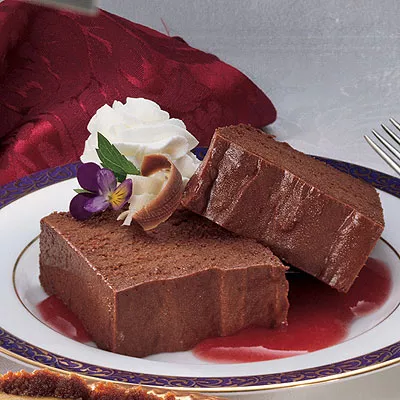 Photograph: two chocolate mousse slices on red sauce, whipped cream and violets