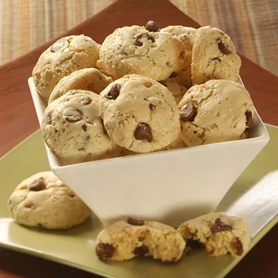 Photograph of a white bowl of chocolate chip cookies on a green plate