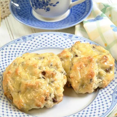 Photograph: two cheesy biscuits with golden melted topping on blue patterned plate, teacup behind