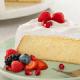 A can of Carnation sits behind a slice of of frosted pound cake topped with berries on a plate with a fork and mixed berries.